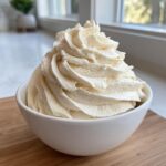 A close-up of perfectly piped, fluffy vanilla buttercream frosting swirling high in a small white bowl.