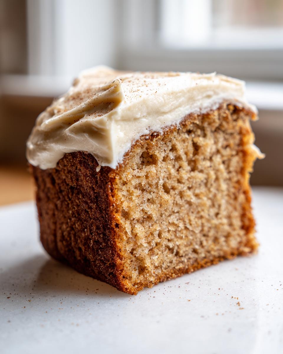 Close-up of a moist slice of applesauce cake topped with thick cream cheese frosting and sprinkled with cinnamon.