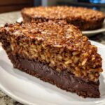 A decadent slice of german chocolate pie showing a rich chocolate bottom layer and a thick coconut-pecan topping.