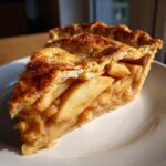 A perfect slice of homemade apple pie showing thick, spiced apple filling and a flaky, golden-brown crust.