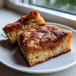 Two square slices of moist snickerdoodle blondies featuring a thick, sugary cinnamon topping served on a white plate.