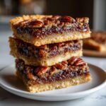 A tempting stack of three gooey pecan pie bars with a shortbread crust, topped with whole pecans.