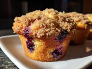 A close-up, sunlit shot of a tender blueberry muffin topped with brown sugar streusel, showing juicy blueberries baked inside.