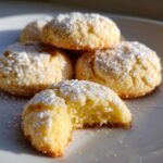 A close-up of several soft 3-ingredient butter cookies stacked on a white plate, one cookie has a bite taken out showing the crumb.