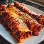 Close-up of three baked cheese enchiladas covered in red sauce and melted, bubbly cheese.