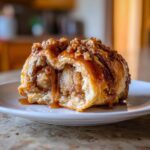 A cross-section of a warm apple dumpling overflowing with spiced apple filling and dripping with rich caramel sauce.
