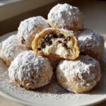 A stack of powdered sugar-dusted cannoli cookies, one cut open to show creamy filling and mini chocolate chips.