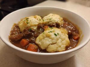 Close-up of a white bowl filled with rich ground beef and dumplings stew, garnished with parsley.