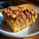 A close-up of a square slice of apple baked oatmeal with a thick, brown sugar crumb topping.