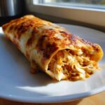 A close-up of a golden-brown Baked Chicken Chimichanga, showing shredded chicken filling spilling out slightly.