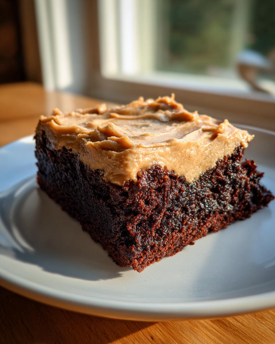 A decadent square of banana bread brownies topped with thick peanut butter frosting, sitting on a white plate.