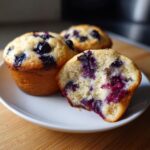 Close-up of a halved blueberry protein muffin showing a moist interior packed with berries.
