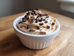 A creamy, light brown peanut butter dip topped generously with mini chocolate chips, served in a white fluted ramekin.