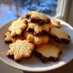 A pile of star-shaped italian butter cookies dipped in dark chocolate resting on a white plate.