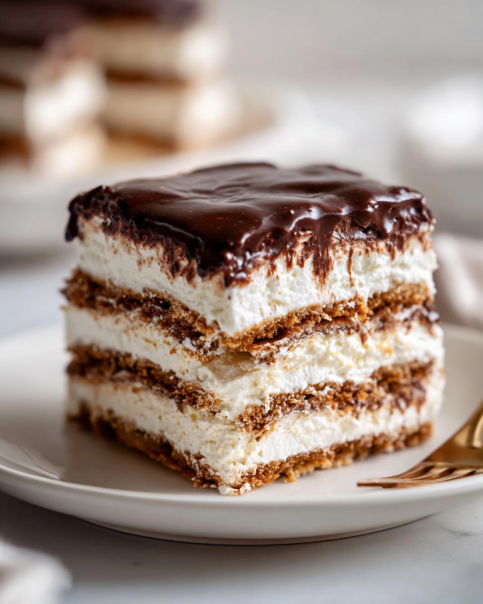 Close-up of a layered slice of chocolate eclair cake showing graham cracker layers, creamy filling, and rich chocolate glaze.