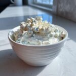 A white bowl filled high with chunky blue cheese dip, featuring visible crumbles of blue cheese.