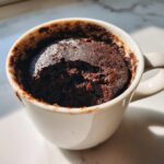 Close-up of a rich, dark chocolate Cottage Cheese Microwave Brownie baked inside a white mug.