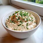 A white bowl filled with creamy clam dip, generously garnished with chopped green chives.