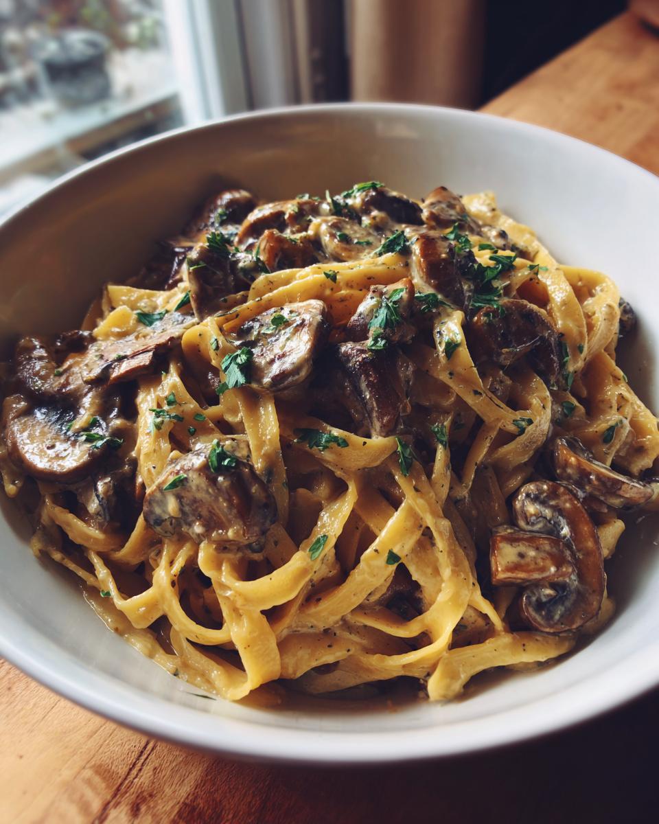 Close-up of creamy mushroom pasta featuring fettuccine noodles coated in a rich sauce and topped with sautéed mushrooms and parsley.