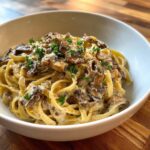 A close-up of creamy fettuccine mushroom pasta topped with sautéed mushrooms and fresh parsley.