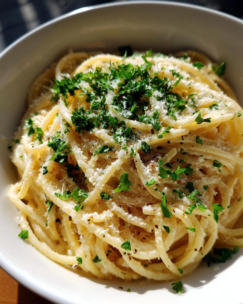 Close-up of a bowl of creamy parmesan pasta topped with grated cheese and fresh chopped parsley.