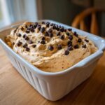 A close-up of a creamy, light brown peanut butter dip generously topped with mini chocolate chips in a white rectangular dish.