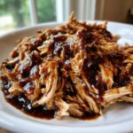 Close-up of moist, shredded crockpot teriyaki chicken generously coated in a thick, dark teriyaki sauce.