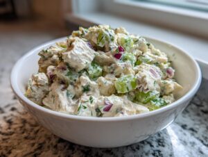 Close-up of a white bowl filled with creamy dill pickle chicken salad featuring chunks of chicken, celery, and red onion.