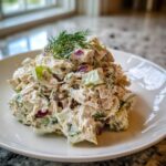 A mound of creamy dill pickle chicken salad mixed with red onion and celery, garnished with fresh dill.