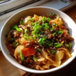 A close-up of a hearty serving of egg roll in a bowl, topped with fresh green onions and sesame seeds.