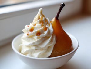 A single, beautifully caramelized poached pear served in a white bowl next to a swirl of whipped cream drizzled with caramel.