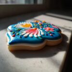 Close-up of a flower-shaped sugar cookie with vibrant blue, hardened sugar cookie icing decorated with floral details.