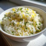 Close-up of fluffy mediterranean rice in a white bowl, garnished with bright green parsley and yellow lemon zest.