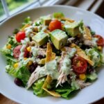 A vibrant bowl of southwest salad featuring shredded chicken, black beans, corn, avocado chunks, and creamy dressing.
