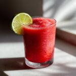 Close-up of a vibrant, frozen strawberry daiquiri garnished with a fresh lime wheel.