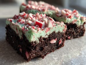 A close-up of a fudgy peppermint brownie slice topped with light green frosting and crushed candy canes.