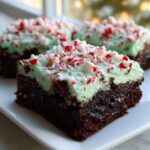 A close-up of a fudgy peppermint brownie topped with light green mint frosting and crushed candy canes.