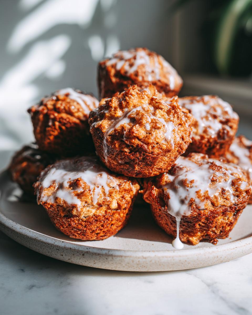 A close-up stack of golden brown baked apple fritters drizzled with white glaze, presented on a speckled plate.