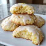 A stack of soft, glazed italian ricotta cookies, one broken open to show the texture, topped with lemon zest.
