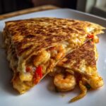 Two golden brown wedges of a perfectly cooked shrimp quesadilla, revealing seasoned shrimp and melted cheese inside.