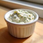 Close-up of creamy homemade tartar sauce, garnished with fresh dill, served in a white fluted ramekin.
