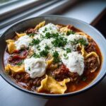 A close-up bowl of rich instant pot lasagna soup topped with dollops of ricotta, parmesan, and fresh parsley.