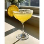 A bright yellow lemon drop martini served in a coupe glass with a thick sugar rim and a fresh lemon wheel garnish.