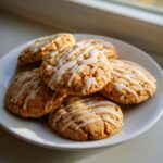 A stack of soft maple brown sugar cookies drizzled with a white vanilla glaze, sitting on a white plate.