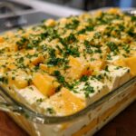 Close-up of cubed orange cheddar and white feta cheese layered in a dish for marinated cheese, topped with fresh parsley.