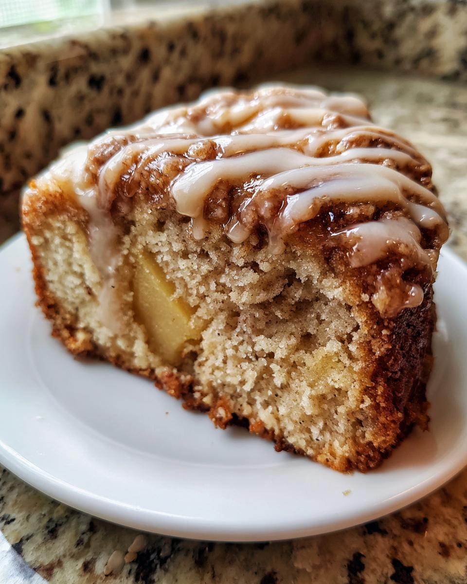 Close-up of a moist slice of apple dapple cake topped with cinnamon streusel and vanilla glaze.
