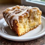 Close-up of a moist slice of apple dapple cake topped with caramelized apples and a white vanilla glaze.