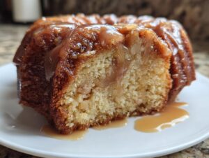 Close-up of a moist slice of apple dapple cake featuring visible apple chunks and a rich caramel glaze dripping onto a white plate.