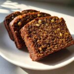 Three thick slices of moist date nut bread, studded with visible walnuts, served on a white plate.