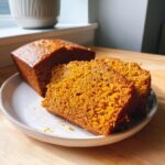 Close-up of moist pumpkin bread loaf with two thick slices cut and displayed on a white plate.